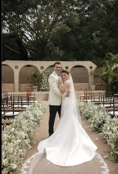 Noivo de smoking branco e noiva no corredor de um casamento ao ar livre